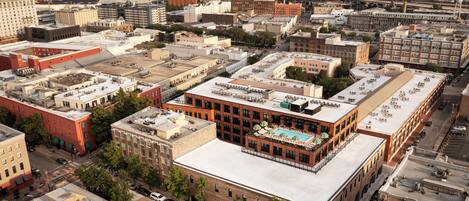 An aerial view of a cityscape with a prominent building featuring a rooftop pool and a large parking lot.