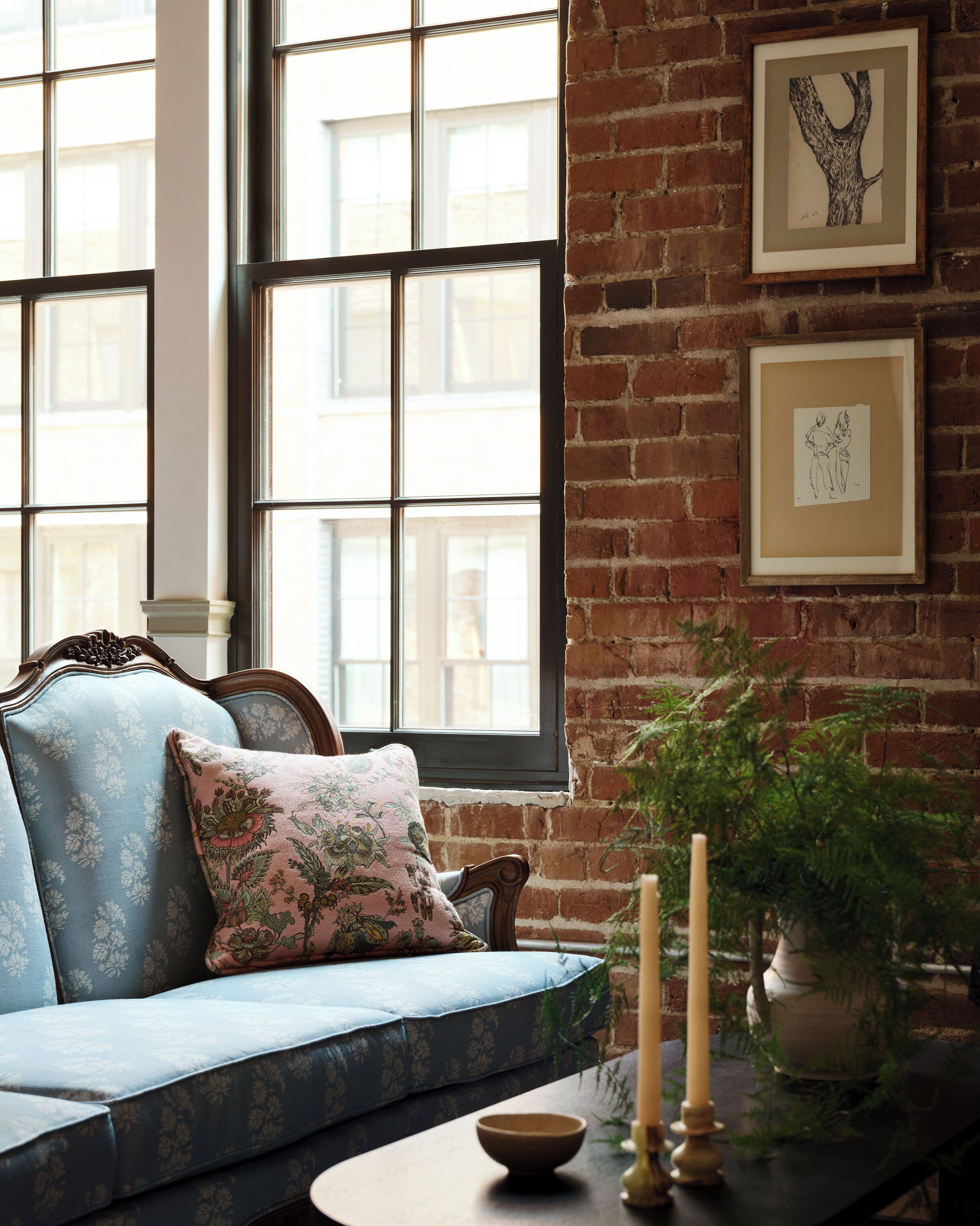 A room with a blue sofa, a wooden table with candles, and a brick wall with framed artwork.