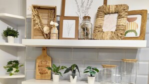 A kitchen with white brick walls, shelves with plants, a wooden cutting board, and framed artwork.