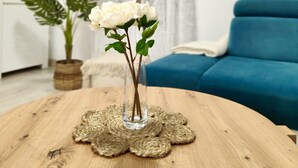 A room with a blue sofa, a wooden table with a vase of white flowers, and a wall decorated with hats and a dreamcatcher.