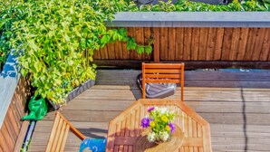 A wooden deck with a table and chairs, surrounded by lush greenery and a wooden fence. - Ferienwohnung Friedrichroda (Friedrichroda)