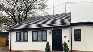 A small, single-story building with a black door and windows, a gravel driveway, and two potted plants in front. - Blackberry Cottage - Cosy Autumn Getaway in Cardiff

 (Cardiff)