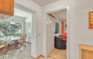 En matplats med ett bord och stolar, ett kök med en röd stol och en hall som leder till en dörr.