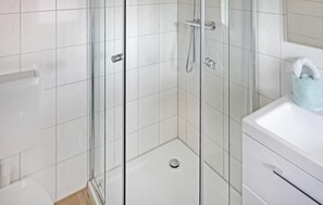 Bathroom features a glass-enclosed shower with handheld showerhead and wall-mounted faucet, alongside a sink with towel holder.
