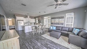 A spacious living area with a gray sofa, a dining table with chairs, a kitchen with white cabinets, and a ceiling fan.