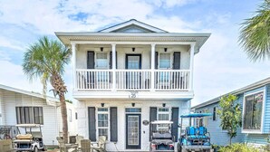 A two-story house with a balcony, a golf cart, and a blue utility vehicle parked in front.