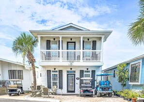 A two-story house with a balcony, a golf cart, and a blue utility vehicle parked in front. - 025 Gulf Dr. - Great 2 Story Home with Golf Cart! 2 Golf Carts! (Panama City Beach)