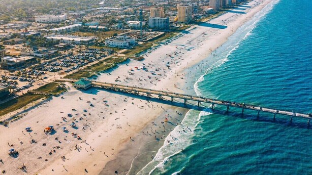 An aerial view of a beach with a pier, buildings, and a coastline. - Lower · 2/1 - Lower Unit - 4 Blocks to the Beach (Jacksonville Beach)