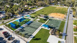 An aerial view of a sports complex with multiple tennis courts, a baseball field, and surrounding residential areas.