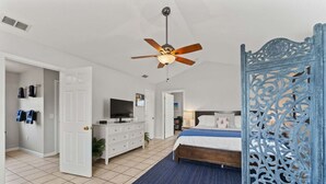 A bedroom with a bed, a ceiling fan, a TV, and a decorative screen.