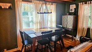 A dining area with a wooden table and chairs, a hanging light fixture, and a cabinet with a geometric pattern.