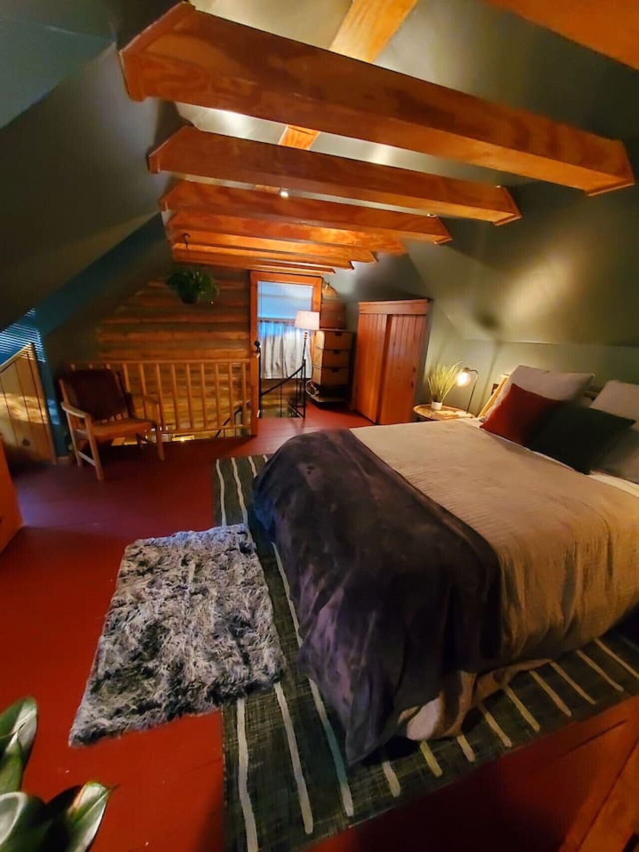 A cozy bedroom with a large bed, a wooden ceiling, and a small seating area with a chair and table.