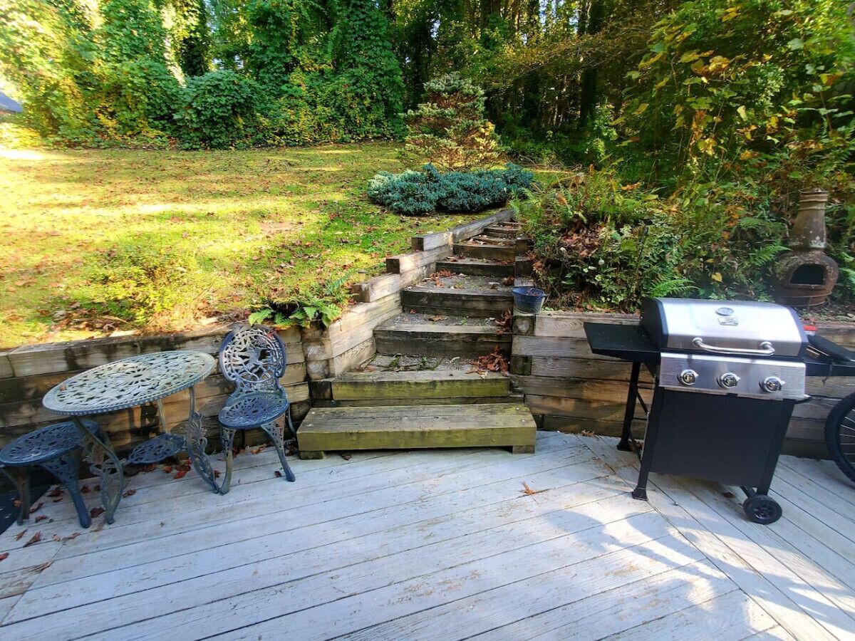 Eine Terrasse mit Grill, zwei Metallstühlen und einem kleinen Tisch.