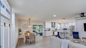 Une cuisine spacieuse avec des meubles blancs, un coin repas avec une table et des chaises en bois, et un salon avec un canapé et des fauteuils.