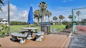 An outdoor patio with a grill, a blue umbrella, and stone tables.