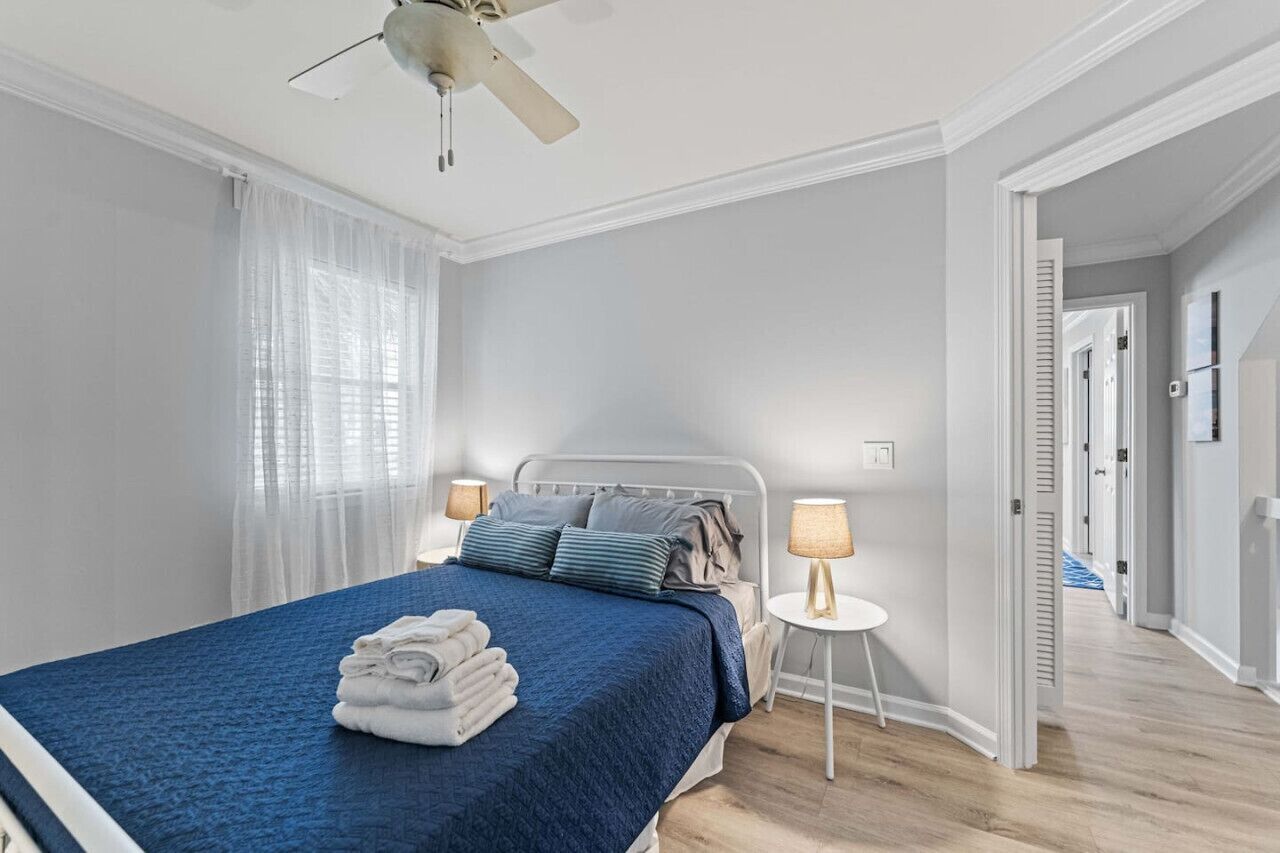 Un dormitorio con cama, lámparas de noche, ventilador de techo y vista a un pasillo.