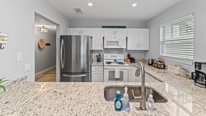 A modern kitchen with white cabinets, stainless steel appliances, granite countertops, and a window with blinds. - Steps 2 Sand! Bch amenities, yard, rooftop & games (Jacksonville Beach)