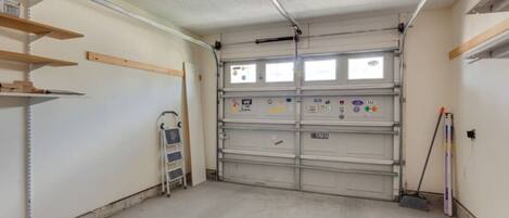 A garage with a closed garage door, metal shelving, a ladder, and a broom.