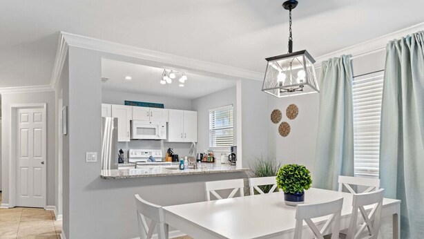 A modern kitchen with white cabinets, a central island, and a dining area with white chairs. - Steps 2 Sand! Bch amenities, yard, rooftop & games (Jacksonville Beach)