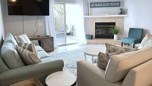 A living room with a flat-screen TV, a fireplace, a ceiling fan, and a sign that reads 'EAT. BEACH. SLEEP. REPEAT.' - Steps 2 Sand! Bch amenities, yard, rooftop & games (Jacksonville Beach)