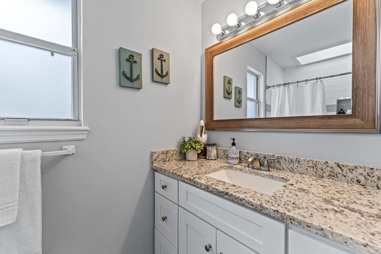 Un baño con lavamanos de encimera de granito, espejo con marco de madera y anclas decorativas en la pared.