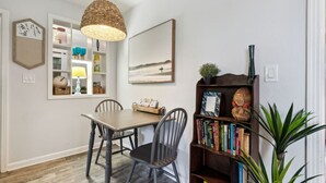 A dining area with a wooden table and chairs, a bookshelf with books, a hanging lamp, and a framed picture on the wall. - 1950's Charmer: Bikes/Games/Hot Tub/Fire Pit (Jacksonville Beach)
