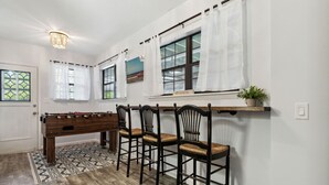 A room with a foosball table, four chairs, a shelf with a plant, and a window with curtains. - 1950's Charmer: Bikes/Games/Hot Tub/Fire Pit (Jacksonville Beach)