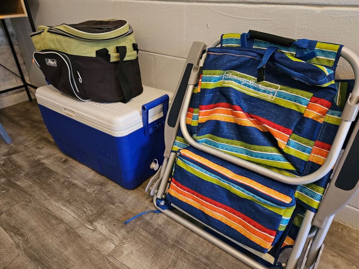 A blue cooler, a black and green bag, and a colorful striped bag on a metal cart.