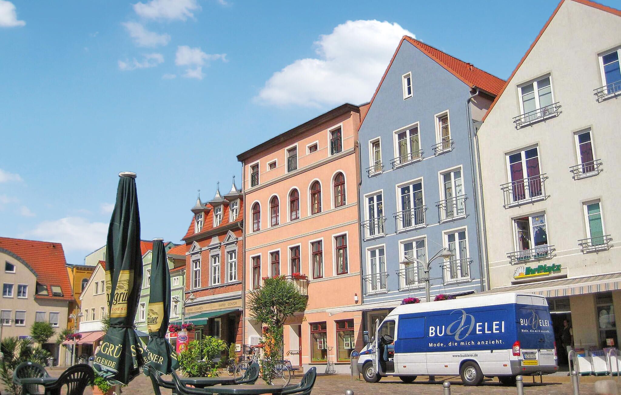 Une rue bordée d’immeubles aux couleurs vives, avec un fourgon garé et des tables installées à l’extérieur.