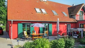 Ein rotes Backsteinhaus mit geneigtem Dach, grünen Fensterläden und einer Terrasse mit Sitzgelegenheiten.