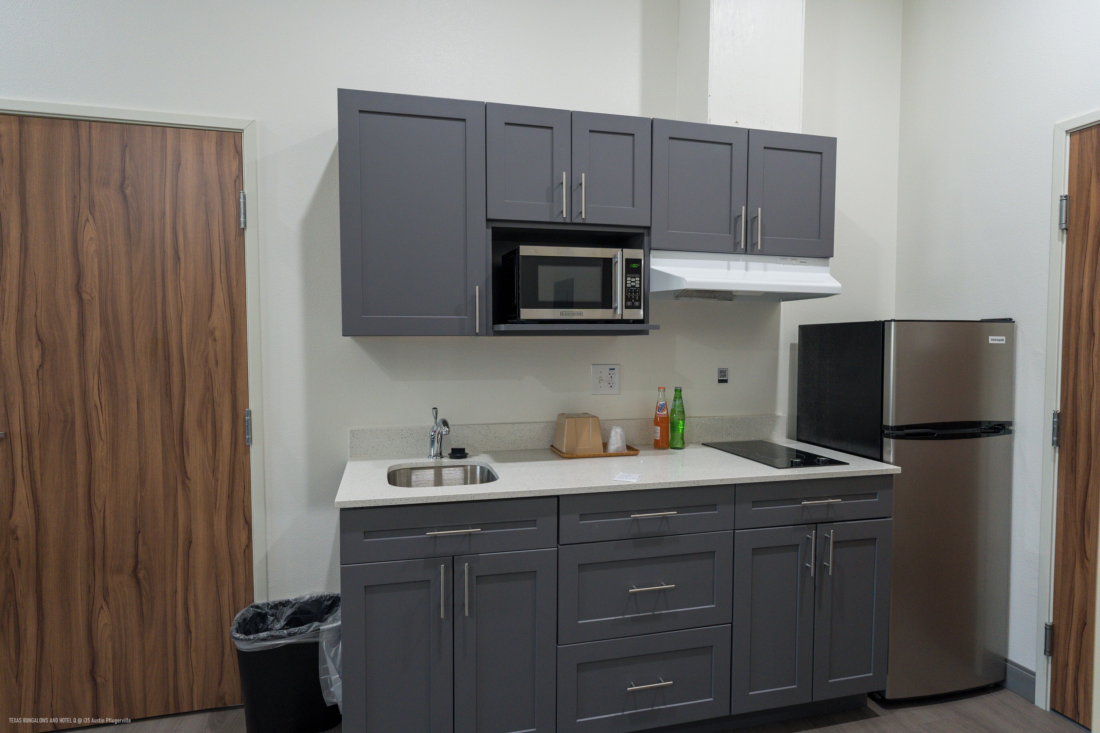 A compact kitchen with grey cabinets, a stainless steel microwave, a built-in oven, and a refrigerator.