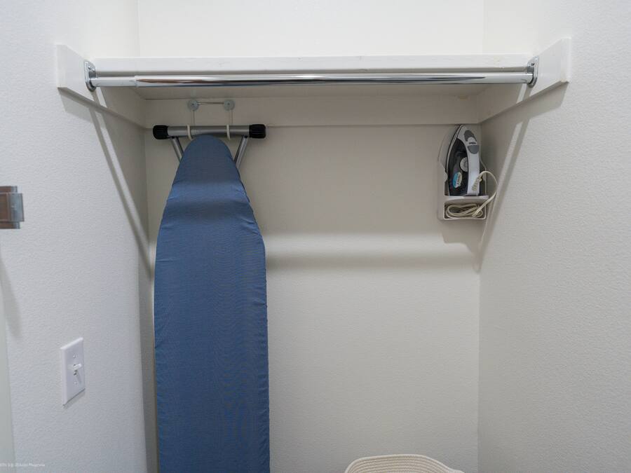 Una habitación pequeña y funcional con una estación de planchado integrada, que incluye un planchador y un tendedero.