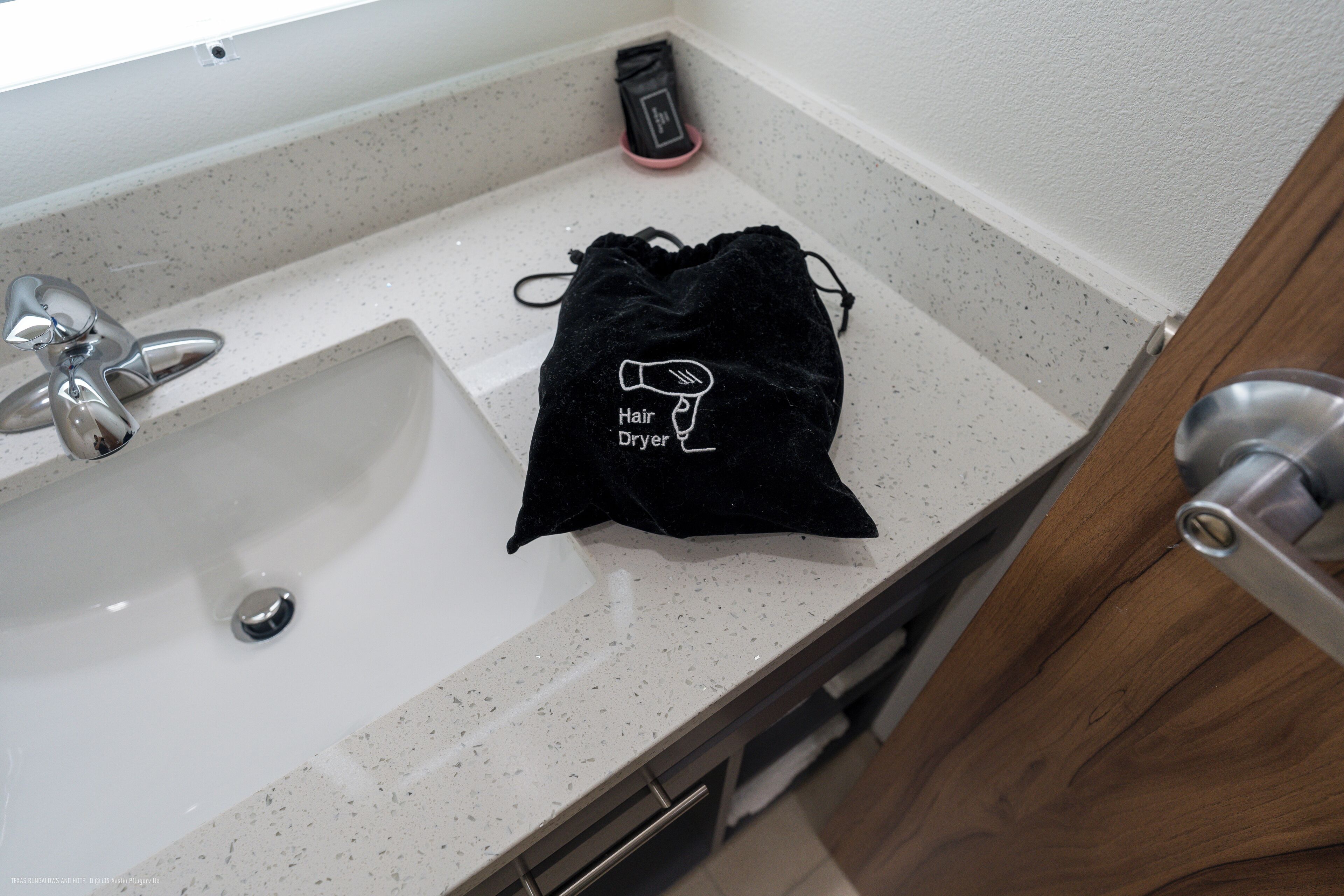 Un lavabo de salle de bain avec un sac noir à cordon de serrage sur le comptoir, sur lequel est écrit « Sèche-cheveux ».