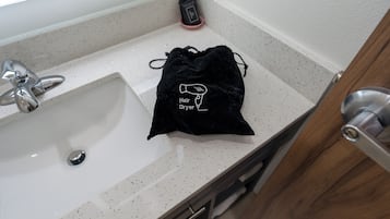 Un lavabo de salle de bain avec un sac noir à cordon de serrage sur le comptoir, sur lequel est écrit « Sèche-cheveux ».