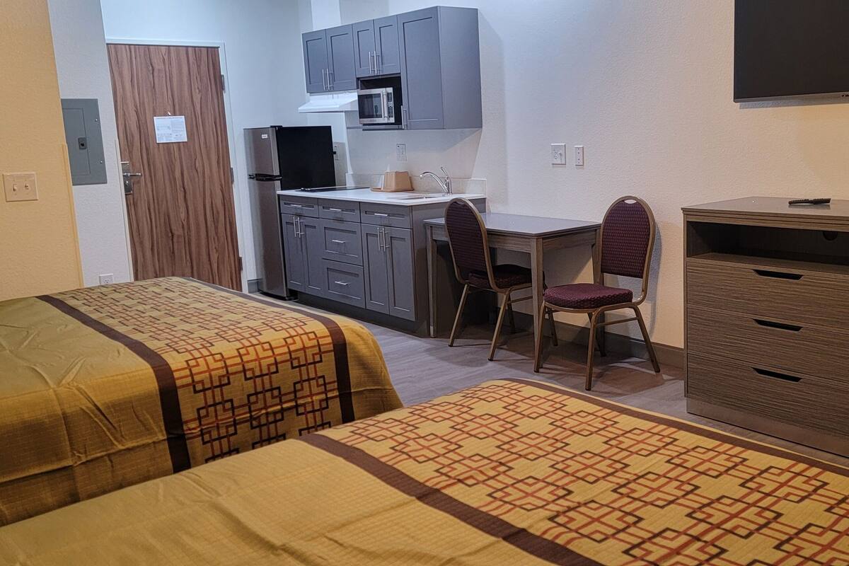 Una habitación con dos camas, un escritorio con silla, microondas y televisión.