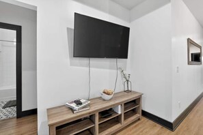 A modern living room with a flat-screen TV mounted on the wall, a wooden console table with a bowl of decorative items, and a framed mirror on the wall. - Two Homes, One Booking | Sleeps 20 | 6BR/4BA Chattanooga Compound | Hot Tub · Pool Table (Chattanooga)
