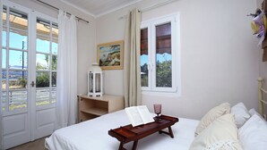 Una camera da letto con un letto, un comodino con un libro e un bicchiere, e una finestra con tende.