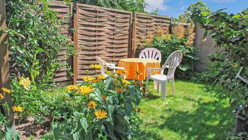 Ein Garten mit Holzzaun, einem Tisch mit gelber Tischdecke und zwei weißen Stühlen.