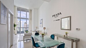 Un salon moderne avec une table à manger en verre, des chaises bleues, un canapé blanc et une grande fenêtre donnant sur la ville.