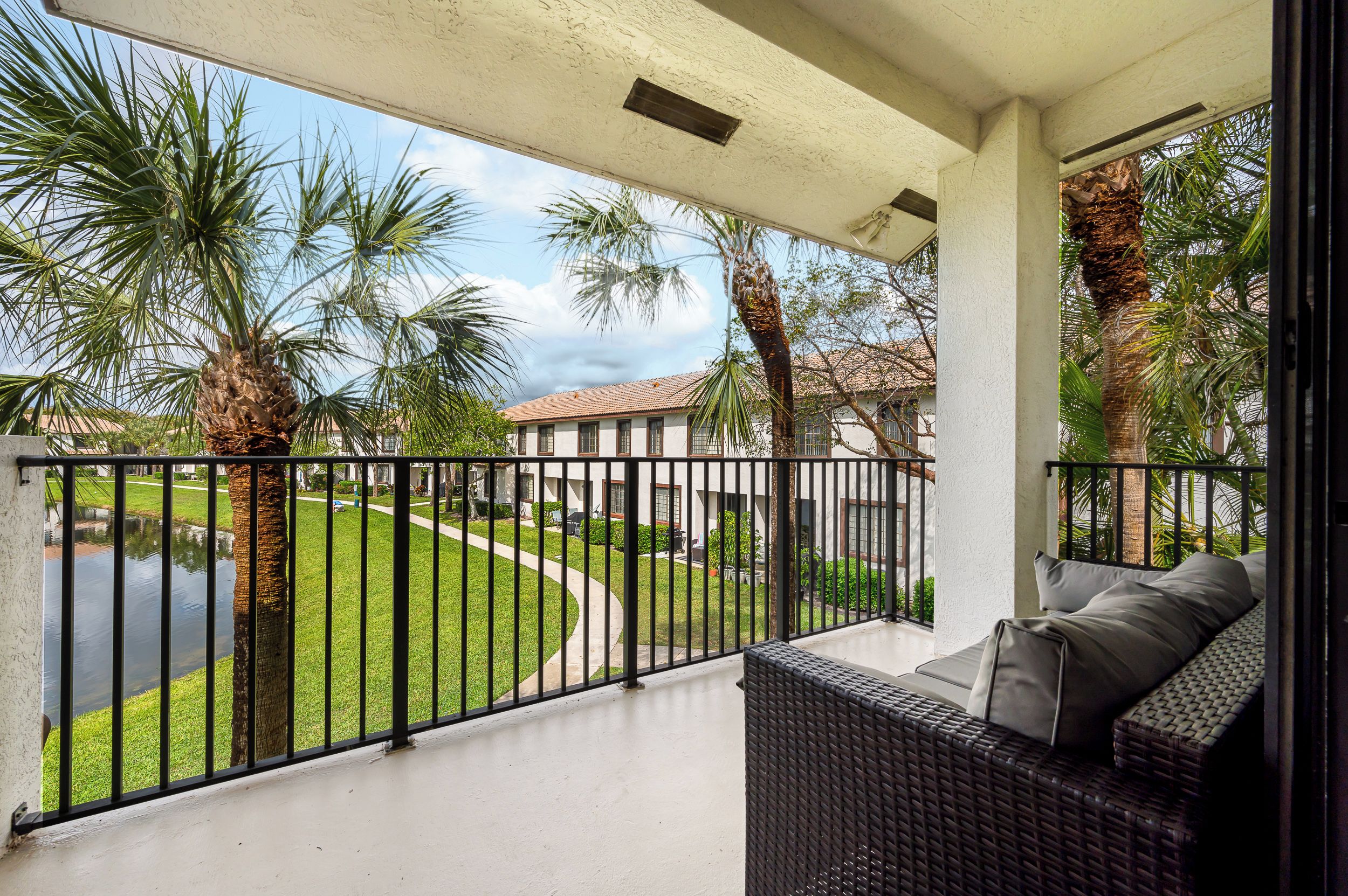 Un balcon avec un canapé en osier et une vue sur un espace paysager agrémenté de palmiers et d’un sentier.