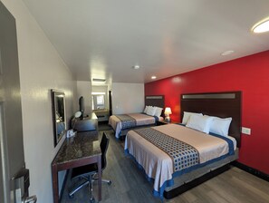 Habitación de hotel con dos camas, un escritorio, una silla, un espejo y una pared roja decorativa.