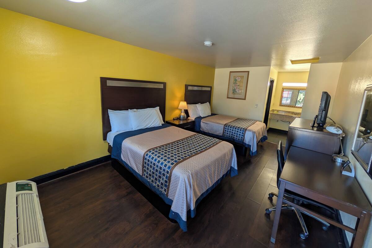 A hotel room with two beds, a desk with a computer, a chair, and a window.