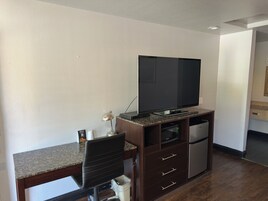 Un espacio habitable compacto con una televisión de pantalla plana sobre un soporte de madera, un refrigerador pequeño, un microondas y una zona de comedor con una silla y una mesa.