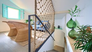 Un escalier avec un filet en corde, des chaises en osier, un canapé bleu et des vases verts placés sur des étagères.
