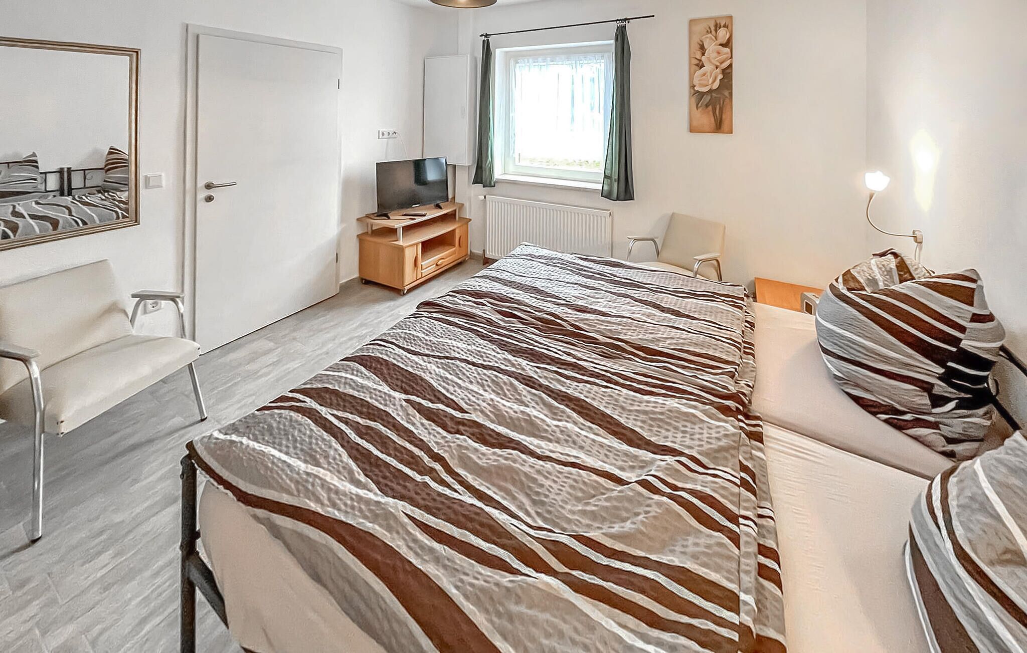 Un dormitorio con cama, televisor, sillón, escritorio y ventana.