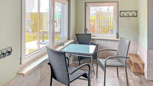 Een hoekappartement met een tafel en vier stoelen, grote ramen en uitzicht op een omheind gazon.