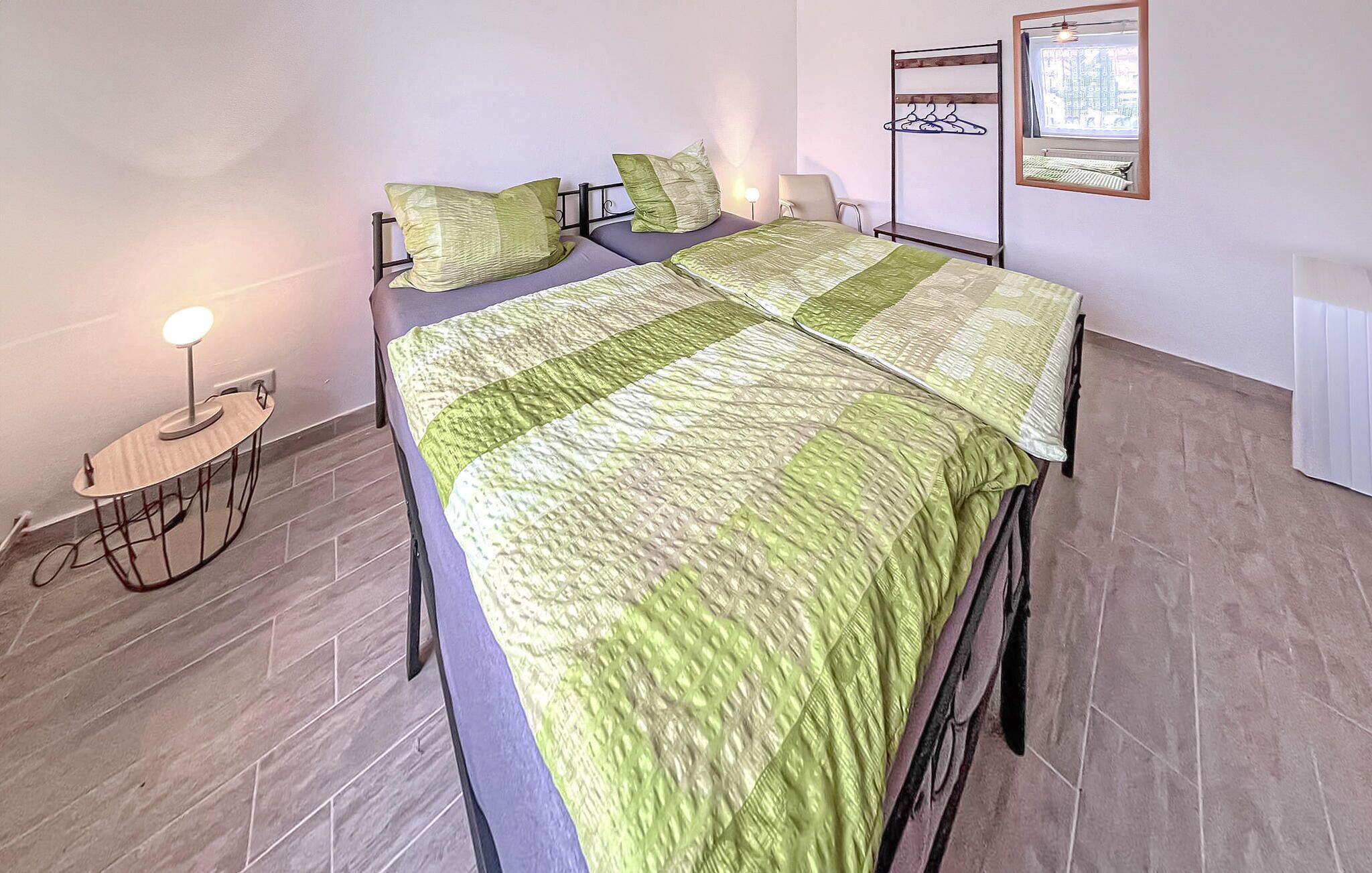 A bedroom with a bed, a bedside lamp, a chair, a coat rack, and a window.