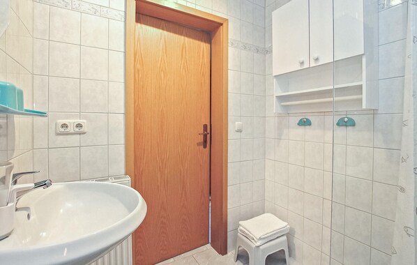 Un baño con puerta de madera, un lavabo blanco, un taburete pequeño y un mueble con espejo.