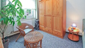 A room with a large wardrobe, wicker furniture, a lamp, and a potted plant.