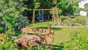 A wooden bench in a garden with a swing set and a ladder.